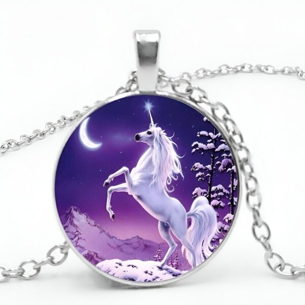 collier-licorne-lune-1a.jpg Un pendentif en forme de cercle avec une image d'une licorne blanche cabrée sur un fond violet avec une lune et des sapins enneigés.