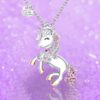 collier-licorne-princesse-3a.jpg L'image représente un collier avec un pendentif en forme de licorne. La licorne est blanche avec une crinière et une queue arc-en-ciel. Elle porte une couronne dorée sur la tête et un collier avec un cœur rose. Le pendentif est en métal argenté et est suspendu à une chaîne en argent.