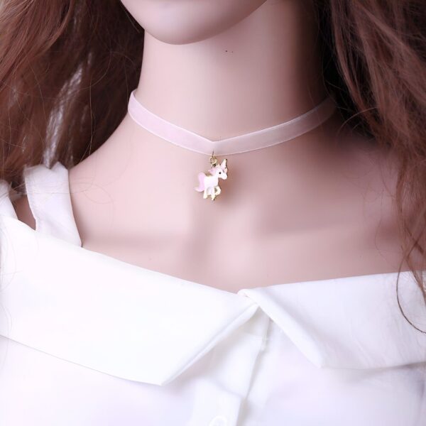 Une jeune femme porte un collier en velours rose avec un pendentif licorne en métal doré. La licorne a une crinière et une queue roses, et des ailes blanches.
