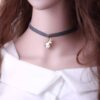 Une jeune femme porte un collier de velours gris avec un pendentif licorne en métal doré. La licorne est blanche et grise avec une crinière et une queue roses.