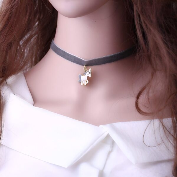 Une jeune femme porte un collier de velours gris avec un pendentif licorne en métal doré. La licorne est blanche et grise avec une crinière et une queue roses.