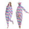 Une femme porte un pyjama licorne arc-en-ciel avec une capuche et une queue. Le pyjama est fait d'un tissu doux et pelucheux et présente des étoiles et des lunes. La femme a les cheveux longs et blonds et elle sourit. Elle porte des chaussettes roses et des pantoufles blanches.