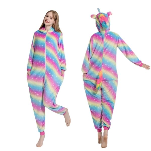 Une femme porte un pyjama licorne arc-en-ciel avec une capuche et une queue. Le pyjama est fait d'un tissu doux et pelucheux et présente des étoiles et des lunes. La femme a les cheveux longs et blonds et elle sourit. Elle porte des chaussettes roses et des pantoufles blanches.