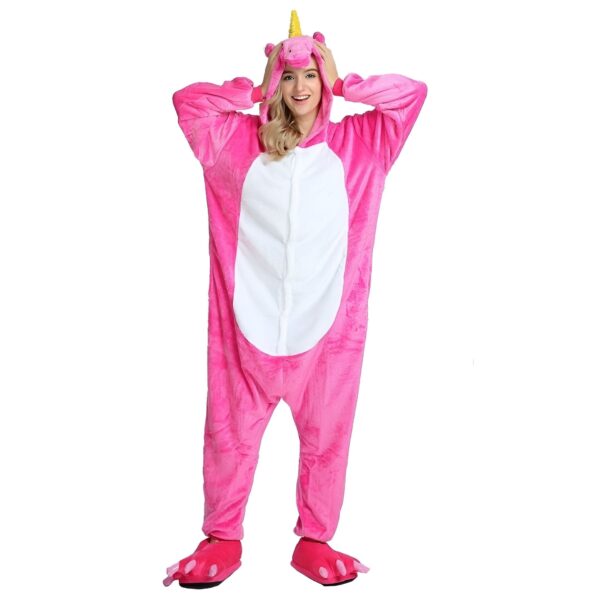 Une femme porte une combinaison pyjama licorne rose avec une capuche et des pieds en forme de pattes de licorne.