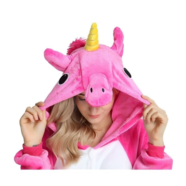 Une femme porte une combinaison pyjama licorne rose et blanche. La combinaison est à capuche avec une corne de licorne jaune sur le dessus de la tête. La femme a les yeux bleus et les cheveux blonds. Elle sourit et regarde l'appareil photo.