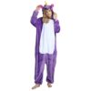 combinaison-licorne-femme-violette-1a.jpg Une femme porte un pyjama licorne violet avec une capuche. Elle a les cheveux blonds et les yeux bleus. Elle est pieds nus et se tient debout dans une position décontractée.