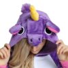 combinaison-licorne-femme-violette-5a.jpg Une femme porte une combinaison pyjama licorne violette avec une capuche. La capuche a une corne jaune, des oreilles roses et des yeux noirs. La combinaison est ouverte sur le devant et l'on peut voir que la femme porte un haut rose en dessous.