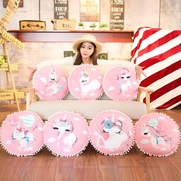 coussin-decoratif-licorne-rose-pour-salon-1a.jpg Une jeune femme souriante assise sur un canapé, entourée de coussins roses décorés de motifs de licornes, chapeau de paille sur la tête. Une décoration intérieure chaleureuse avec des éléments comme des plantes et des panneaux décoratifs en arrière-plan., 45501068837119 | Licorne Shop