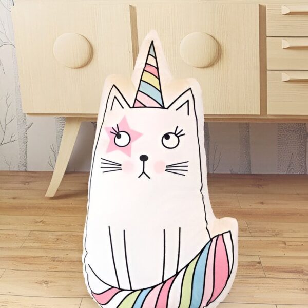 coussin-doux-deco-licorne-chat-1a.jpg Coussin décoratif en forme de chat licorne blanc avec une étoile rose sur l'œil, une corne rayée multicolore et une queue assortie, posé devant un buffet en bois clair dans une chambre d'enfant., 45501065167103 | Licorne Shop