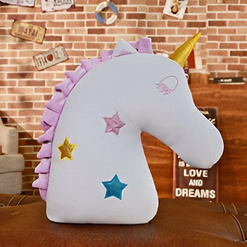 Image d'un coussin décoratif en forme de licorne. La licorne est de couleur claire avec une crinière violette et une corne dorée. Des étoiles colorées décorent son corps. Le coussin est posé sur un canapé devant un mur avec des décorations murales. , 45501065462015 | Licorne Shop