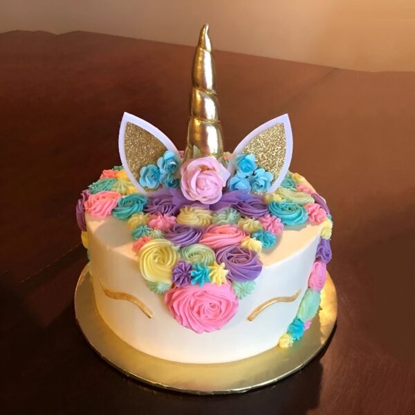 Une image d'un gâteau licorne avec une corne dorée, des oreilles et des fleurs en pâte à sucre colorée.
