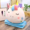 ensemble-coussin-et-couverture-polaire-licorne-enfant-1a.jpg Peluche licorne ronde avec crinière arc-en-ciel et joues roses reposant sur une couverture bleue, avec des décorations floues en arrière-plan., 45501048783103 | Licorne Shop