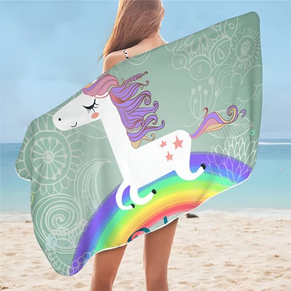 grande-serviette-de-plage-licorne-arc-en-ciel-1a.jpg Femme à la plage, enveloppée dans une serviette avec un motif de licorne blanche sur un arc-en-ciel, sur un fond menthe avec des motifs floraux., 45501254828287 | Licorne Shop