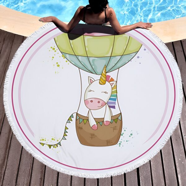 Serviette de plage ronde avec dessin d'une licorne dans une montgolfière, posée près d'une piscine. Une personne est allongée à côté de la serviette., 45501254533375 | Licorne Shop