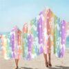 grande-serviette-de-plage-licorne-douce-et-absorbante-1a.jpg Deux personnes sur la plage portent des serviettes à capuche colorées à rayures arc-en-ciel ornées de motifs de licornes blanches et d'étoiles., 45501254893823 | Licorne Shop