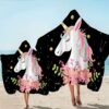 grande-serviette-de-plage-licorne-pour-enfant-1a.jpg Deux personnes à la plage portent des couvertures à capuche décorées de motifs d'unicorne, de fleurs et d'étoiles. Le fond est noir avec des touches dorées., 45501225697535 | Licorne Shop