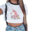 haut-court-pour-femme-imprime-licorne-little-island-1a.jpg Gros plan d'un T-shirt court blanc orné d'un motif de licorne rose et de fleurs colorées. Le t-shirt est porté par une femme en jean taille basse, avec une bretelle noire visible sur l'épaule., 45501297623295 | Licorne Shop