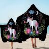Deux personnes sur la plage portant des serviettes à capuche noires avec un motif de licorne blanche, des fleurs colorées, des étoiles, un croissant de lune et des nuages. Idéal pour les enfants et les adultes après la baignade., 45501226090751 | Licorne Shop