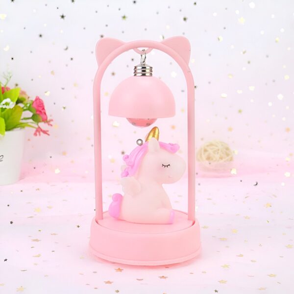lampe-de-chevet-licorne-rose-2a.jpg Une veilleuse rose en forme de licorne avec des ailes et une crinière dorée. La licorne est allongée sur un nuage et est entourée d'étoiles.