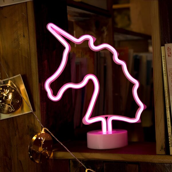 lampe-neon-licorne-1a.jpg Une enseigne lumineuse en forme de licorne rose est posée sur une étagère en bois.
