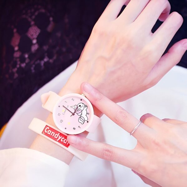 montre-licorne-kawaii-rose-1a.jpg Une personne porte une montre rose avec un lapin blanc dessus. Le bracelet de la montre est blanc avec des écritures rouges "Candycat".