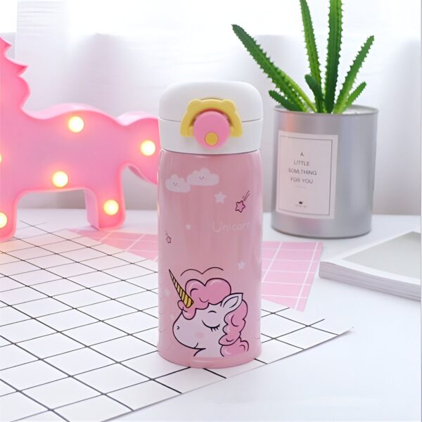 mug-isotherme-licorne-rose-1a.jpg Une bouteille isotherme rose avec une licorne imprimée dessus. La bouteille est posée sur une table à côté d'une plante verte et d'une lampe rose en forme de nuage.