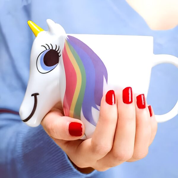 mug-licorne-qui-change-de-couleur-1a.jpg Personne tenant une tasse de café en forme de licorne blanche avec une crinière arc-en-ciel, des ongles rouges et un fond bleu., 45501188407551 | Licorne Shop