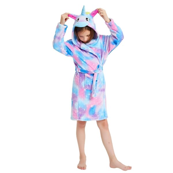 peignoir-de-bain-licorne-fille-1a-1.jpg Une jeune fille porte une robe de chambre licorne. La robe de chambre est rose et bleue avec une capuche licorne. La fille a les cheveux bruns et les yeux bleus. Elle est pieds nus et se tient debout sur un fond blanc.