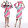 peignoir-licorne-ado-fille-1a.jpg Une jeune fille porte une robe de chambre licorne rose et arc-en-ciel avec une capuche. La robe de chambre est à manches longues et a une ceinture à la taille. La capuche est doublée de polaire rose. La jeune fille est pieds nus et a les cheveux longs et blonds. Elle sourit et regarde l'appareil photo.