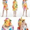 peignoir-licorne-adulte-original-3a-1.jpg Une femme porte une robe de chambre licorne. La robe de chambre est jaune et rose avec une capuche licorne. La femme est debout dans une position de mannequin.