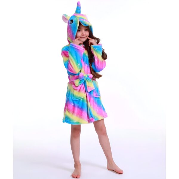 peignoir-licorne-enfant-arc-en-ciel-1a.jpg Une jeune fille porte une robe de chambre licorne arc-en-ciel à capuche. Elle a les cheveux longs et bruns et sourit à la caméra.