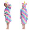 Une jeune fille porte une robe de chambre licorne arc-en-ciel avec une capuche. La robe de chambre est en peluche et a des étoiles blanches. La capuche a une corne de licorne et des oreilles de licorne. La jeune fille est debout et regarde vers la caméra.