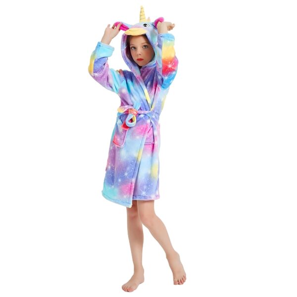 peignoir-licorne-enfant-design-a-capuche-1a.jpg Une jeune fille porte une robe de chambre licorne. La robe de chambre est rose et violette avec une capuche licorne. La fille a les cheveux longs et blonds et elle sourit.
