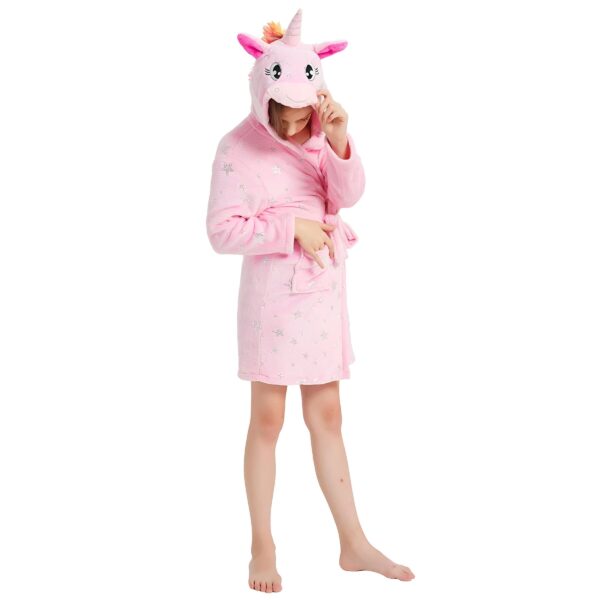 peignoir-licorne-enfant-rose-en-coton-1a.jpg Une jeune fille porte une robe de chambre rose à capuche en forme de licorne. La robe de chambre est ouverte et l'on peut voir qu'elle est doublée de polaire. La capuche est également doublée de polaire et possède une crinière arc-en-ciel. La jeune fille a les cheveux longs et blonds et elle sourit.