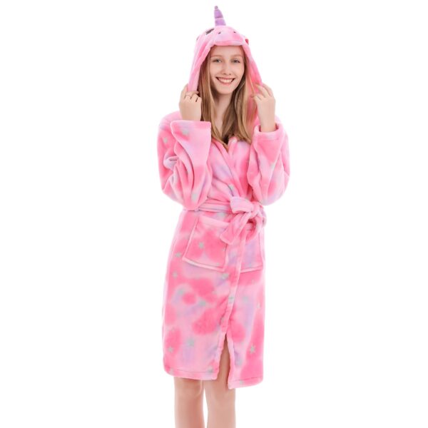 Une jeune fille porte un peignoir rose à capuche avec des étoiles et une licorne.