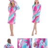 Une jeune fille porte une robe de chambre licorne rose et violette. La robe de chambre a une capuche avec une corne de licorne et des étoiles. La robe de chambre est également dotée de deux poches et d'une ceinture.