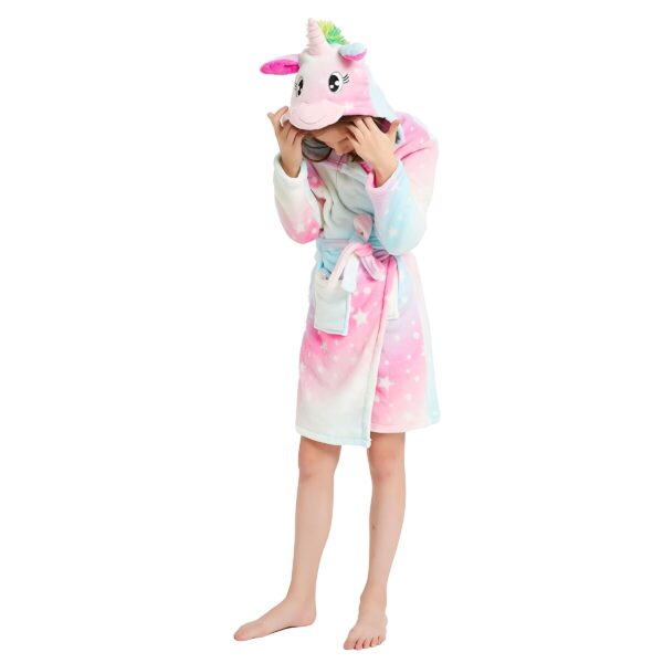 peignoir-licorne-fille-couleur-pale-4a.jpg Une jeune fille porte une robe de chambre licorne rose et bleue avec une capuche. La robe de chambre est en peluche et a des étoiles et des lunes imprimées. La capuche a une corne de licorne et des oreilles.