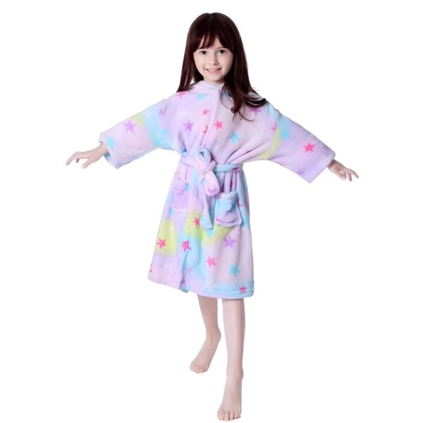 peignoir-licorne-fille-etoile-5a.jpg Une jeune fille porte une robe de chambre licorne violette avec des étoiles multicolores. Elle a les cheveux bruns et les yeux marrons. Elle est pieds nus et se tient debout, les bras ouverts.