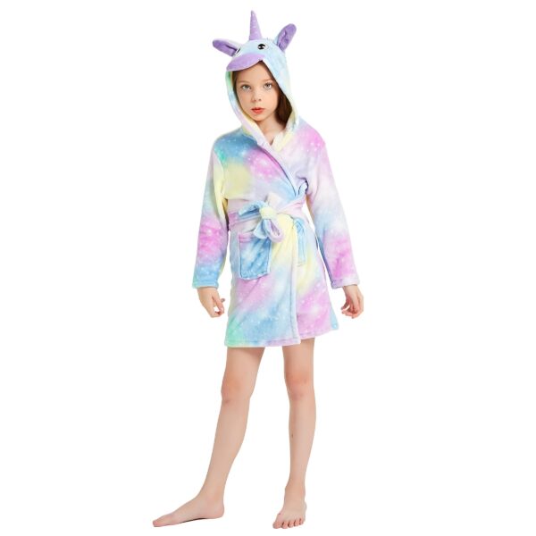 peignoir-licorne-fille-galaxie-en-coton-1a.jpg Une jeune fille porte une robe de chambre licorne. La robe de chambre est rose et violette avec une capuche en forme de tête de licorne. La fille a les yeux bleus et les cheveux blonds. Elle est pieds nus et se tient debout dans une position décontractée.