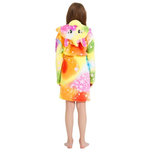 Une jeune fille porte une robe de chambre licorne arc-en-ciel avec une capuche. La robe de chambre est en peluche et a des étoiles et des lunes imprimées. La capuche a une trompe d'éléphant et des oreilles de lapin. La jeune fille est vue de dos.