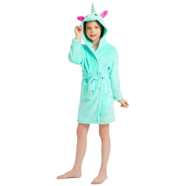 peignoir-licorne-fille-vert-en-coton-1a.jpg Une jeune fille porte une robe de chambre licorne verte à capuche. La robe de chambre est ouverte et l'on peut voir qu'elle est doublée de polaire rose. La capuche est également doublée de polaire rose et a des oreilles de licorne. La robe de chambre est nouée à la taille par une ceinture.