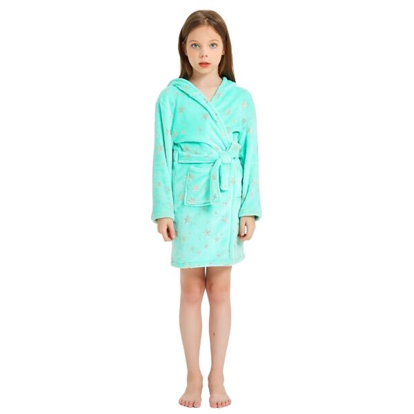 peignoir-licorne-fille-vert-en-coton-4a.jpg Une jeune fille porte un peignoir à capuche vert menthe avec des étoiles argentées. Elle est pieds nus et a les cheveux longs et blonds.