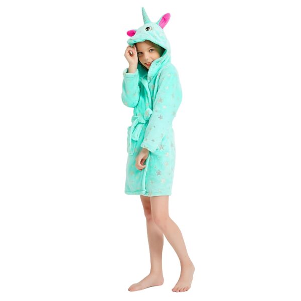peignoir-licorne-fille-vert-en-coton-6a.jpg Une jeune fille porte une robe de chambre licorne verte à capuche. La robe de chambre est ouverte et l'on peut voir qu'elle est doublée de polaire rose. La capuche est également doublée de polaire rose et a une petite corne de licorne sur le dessus. La robe de chambre est parsemée d'étoiles argentées.