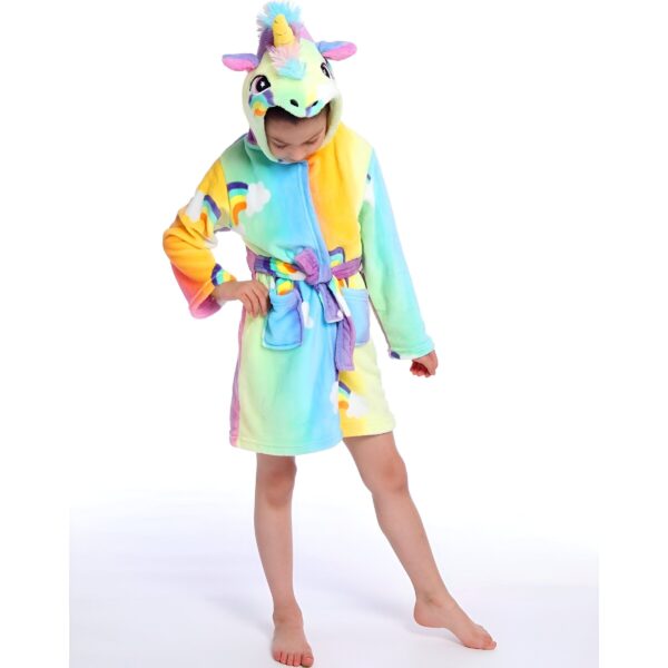 peignoir-licorne-motif-arc-en-ciel-1a.jpg Une jeune fille porte une robe de chambre licorne. La robe de chambre est arc-en-ciel avec une capuche licorne. La fille a les cheveux longs et blonds et elle sourit.