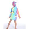 Une jeune fille porte une robe de chambre licorne arc-en-ciel avec une capuche. La robe de chambre est rose, violette et bleue avec des nuages blancs et des arcs-en-ciel. La capuche est en forme de tête de licorne avec une corne et des oreilles.