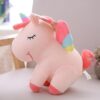 Une peluche licorne rose avec des ailes arc-en-ciel et une crinière arc-en-ciel.