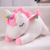 peluche-licorne-couchee-blanche-1a.jpg Une peluche licorne blanche et rose allongée sur un lit avec les yeux fermés. La peluche a une crinière et une queue roses, ainsi qu'une corne multicolore.