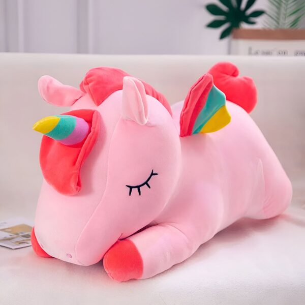 peluche-licorne-couchee-rose-1a-1.jpg Une peluche licorne rose avec une crinière et une queue arc-en-ciel. La peluche est allongée sur le côté et a les yeux fermés.