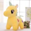 Une peluche licorne jaune avec une crinière et une queue verte. Elle a des yeux roses et noirs et des cœurs multicolores sur le corps.