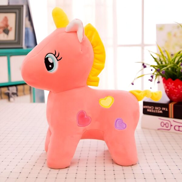 peluche-licorne-orange-enfant-1a.jpg Une peluche licorne rose avec une crinière et une queue jaunes. Elle a des yeux bleus et trois cœurs sur le corps.